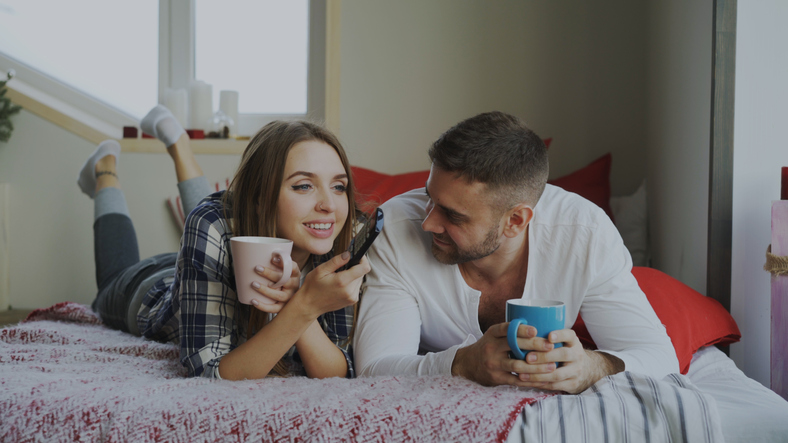 Smiling couple watching TV while lying in bed.