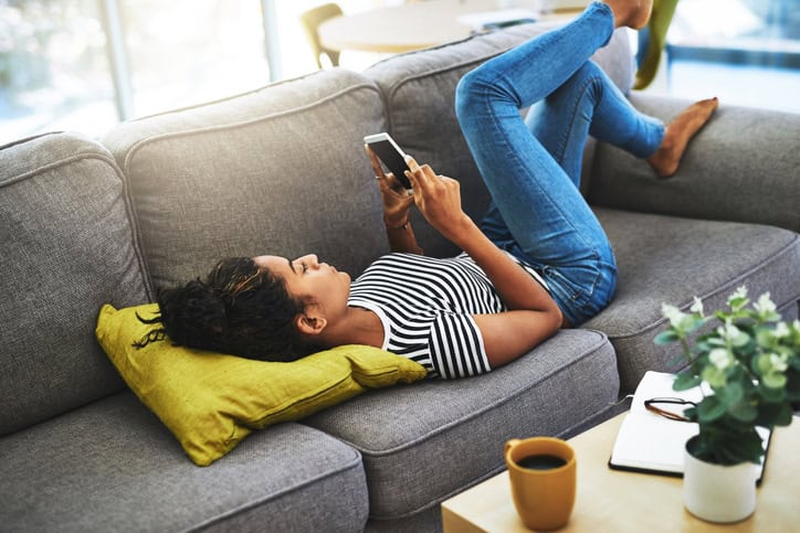 black woman laying couch using mobile