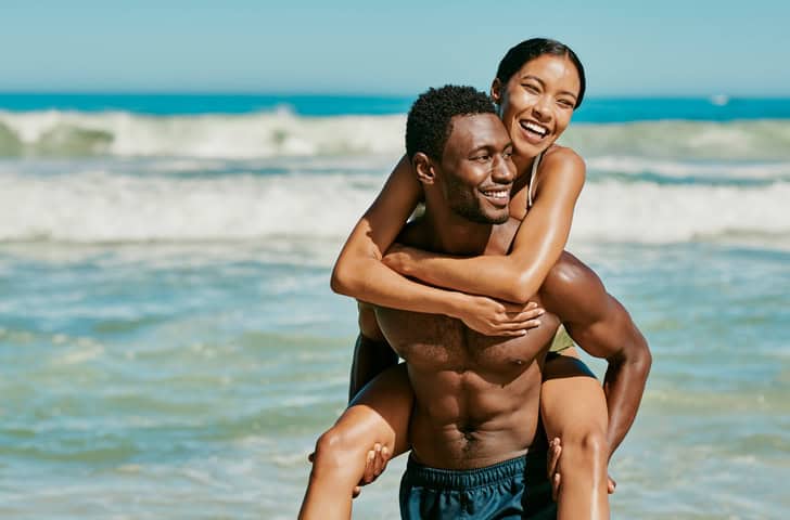 Woman piggybacking with her boyfriend at beach.