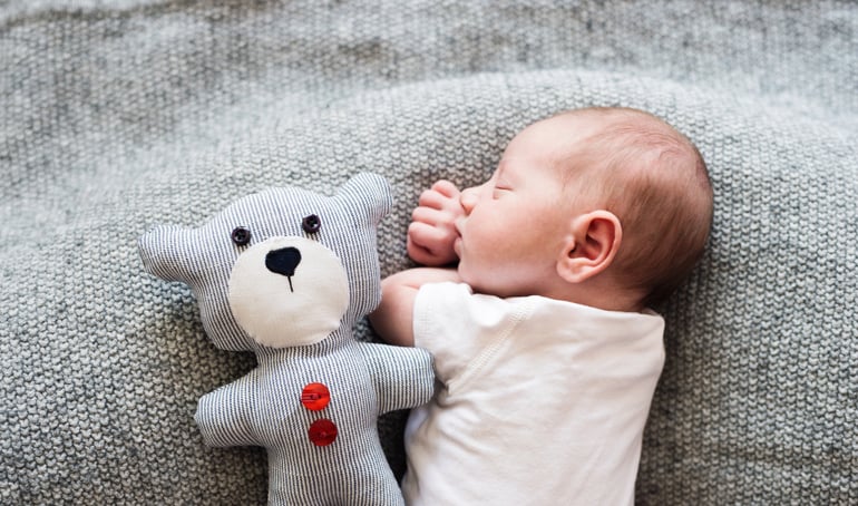 Newborn baby boy lying in bed with teddy bear.