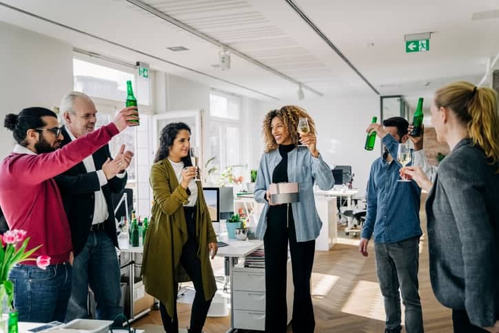 Business people having a party at office. Multi-ethnic business people raising beer bottles and wineglasses during a farewell party of a colleague at work.