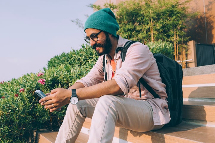 hipster man texting outdoors sitting on step