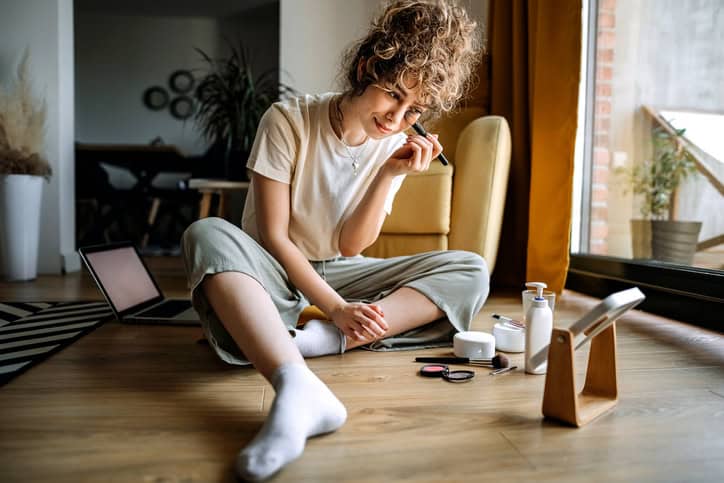 Woman is sitting in her living room and putting on make-up.