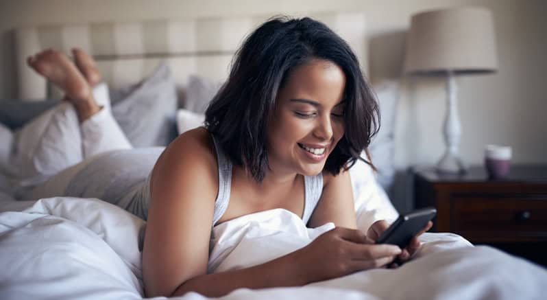 Smiling woman texting in bed.