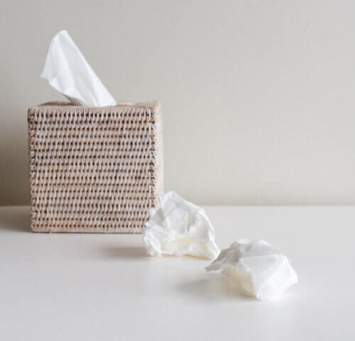 Rattan tissue box and crumpled tissues on table.