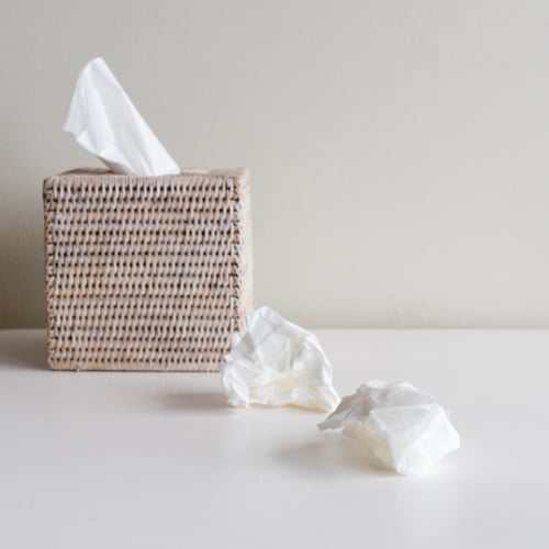 Rattan tissue box and crumpled tissues on table.