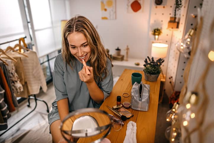 Woman applying lip balm looking in mirror.