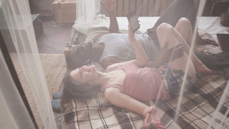 Young couple in pajamas lying on the bed and listening to music. 
