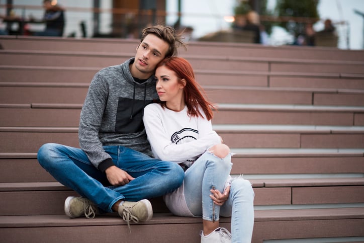 Young couple hugging while sitting on the stairs and looking away in the same direction
