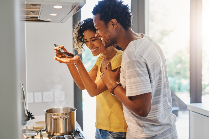 Married couple cooking at home, taste testing the food.