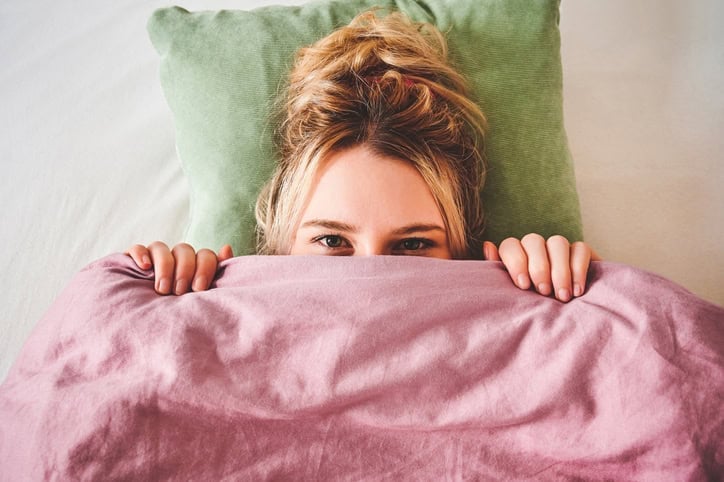 woman peeping over bed covers