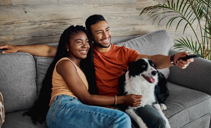 Shot of a happy young couple sitting on the sofa at home with their Border Collie and watching television