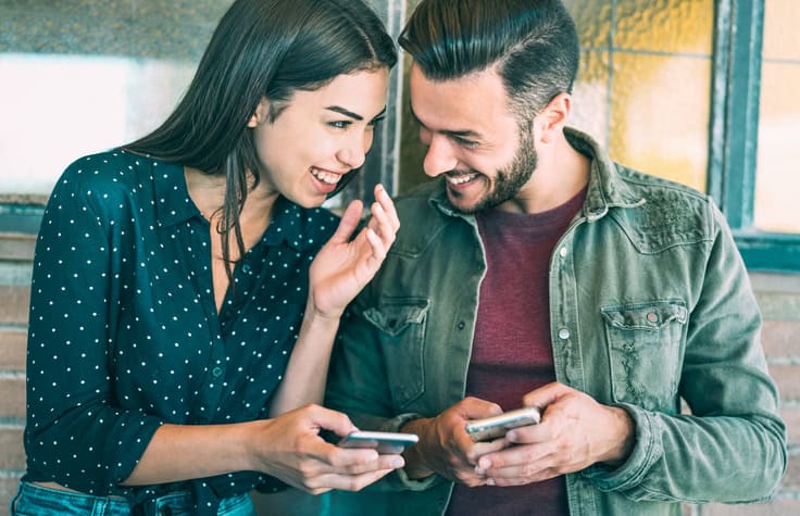 Happy young couple having fun with mobile phones.