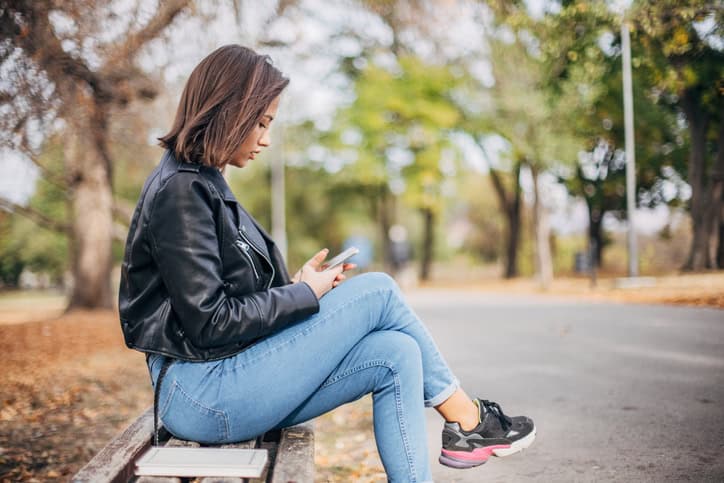 Woman sitting serious on a bench texting