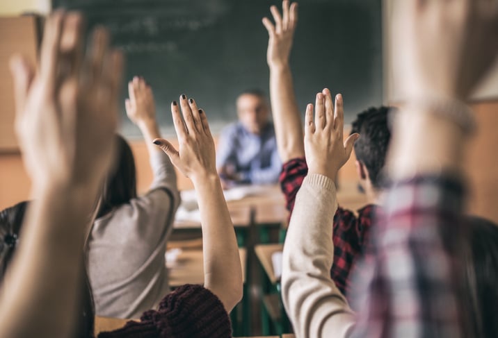 People in a classroom with their hands raised.