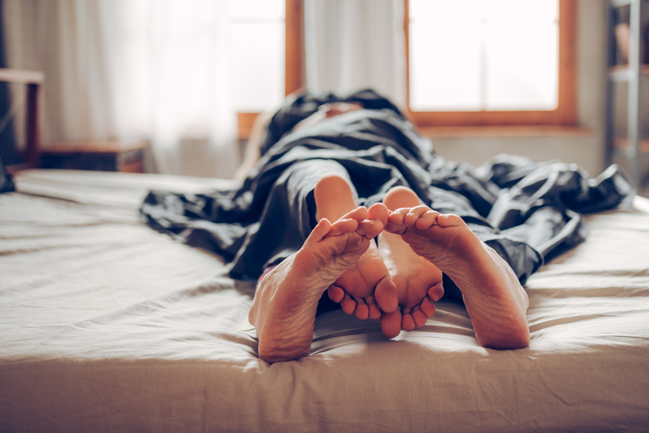 Adult couple's feet laying in bed.