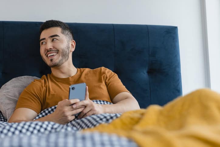happy man texting in bed