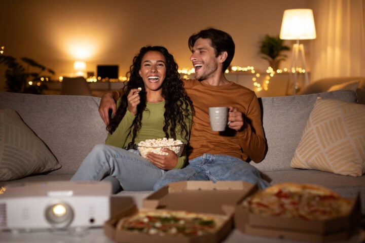 smiling couple watching movie while eating pizza and popcorn,