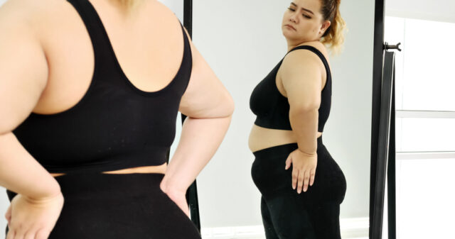 overweight woman scrutinizing appearance in mirror