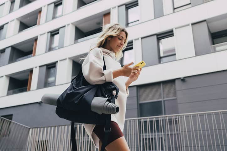 woman texting while walking with yoga mat
