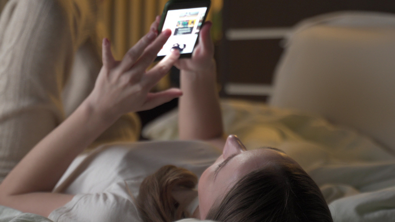 Woman scrolling social media in bed.