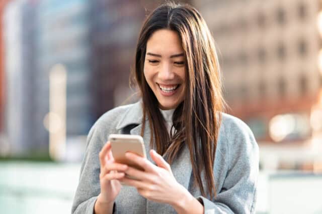 woman laughing while texting on street