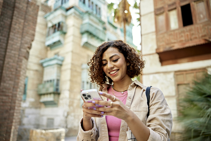 Woman smiling and texting in a Middle Eastern city.
