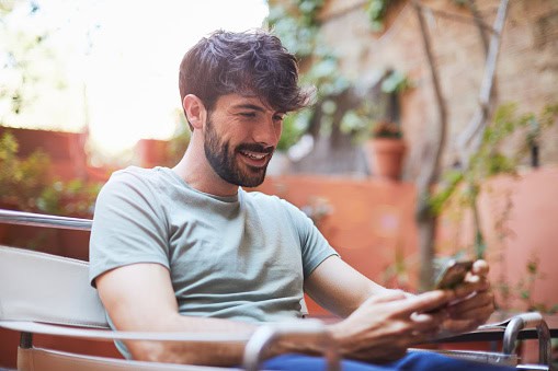One man relaxing at home's terrace texting with a smart phone.