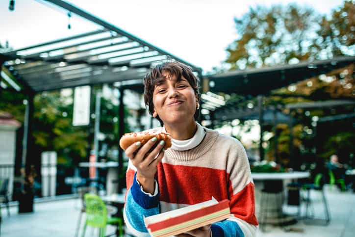 Smiling woman eating hot dog.