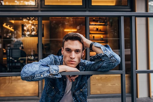 Handsome young man in denim jacket standing outdoors.