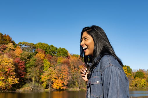 This is a portrait of an Asian American woman in her 30s of Indian ethnicity smiling and laughing as she spends time by the lake in the Catskill Mountains on the Stone Ridge Orchard Farm in upstate New York.