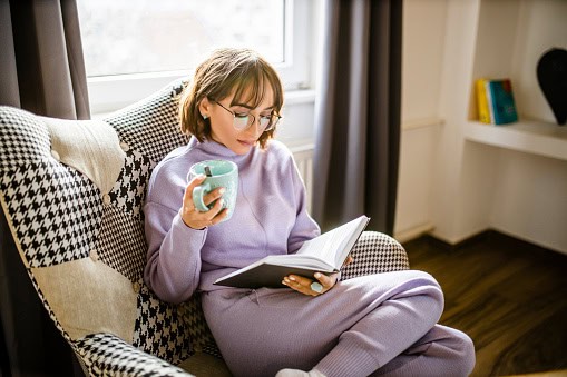 Woman relaxing with book and coffee at home.