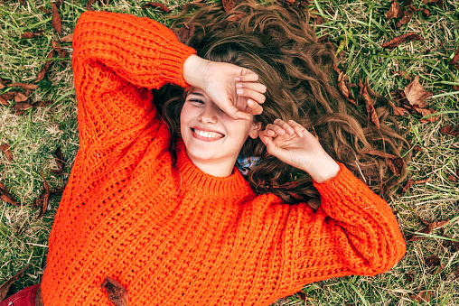 Young woman wearing a knitted orange sweater lying on the grass.