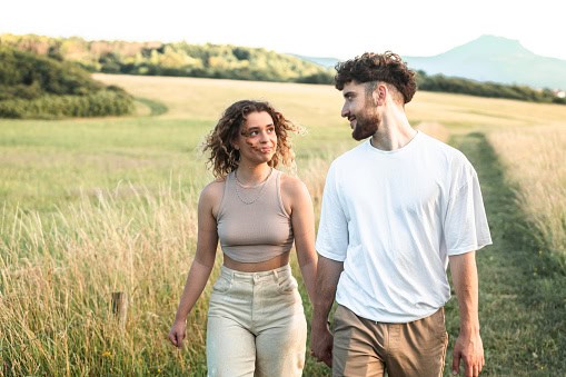 Lovely heterosexual couple in a grass field walking and kissing