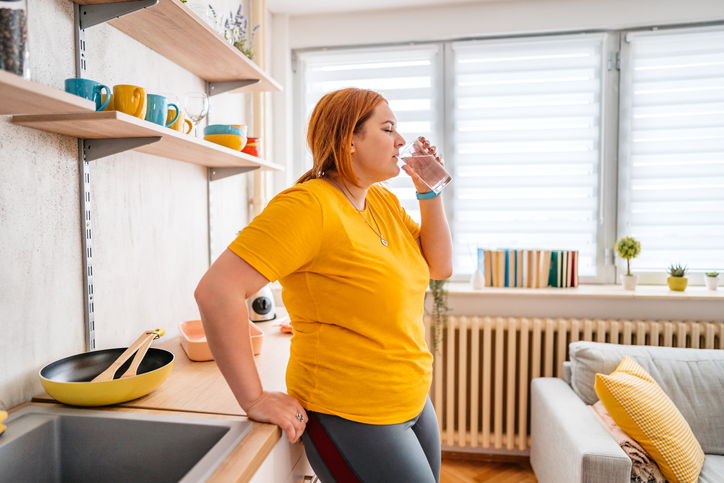 overweight woman in kitchen drinking water.