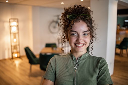 Portrait of a beautiful young smiling teenage girl standing in a cafe with her arms crossed and looking at the camera