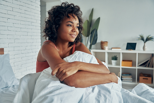 Beautiful young African woman enjoying lazy time in bed after waking up