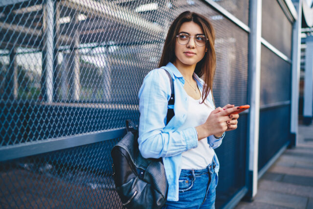 millennial woman texting by fence outdoors