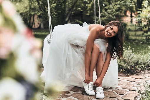 Woman in wedding dress putting on sports shoes and smiling.
