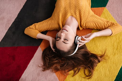 Young girl in headphones enjoying music while lying on a carpet.
