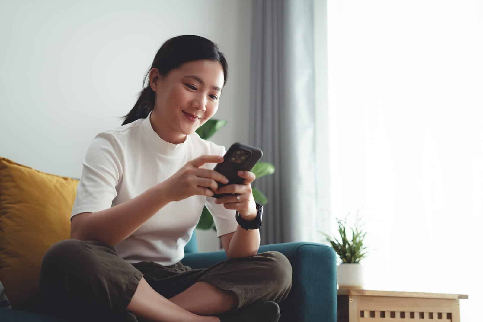 woman smiling while texting on couch
