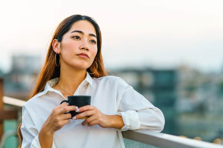 thoughtful woman with coffee on rooftop