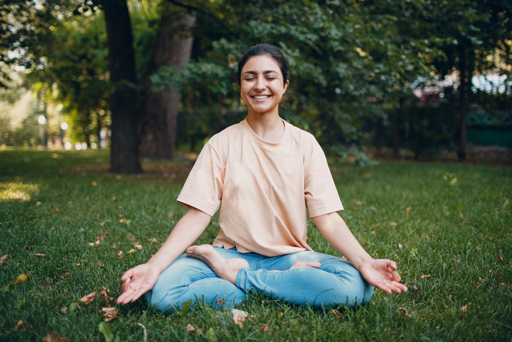 Smiling woman meditating on grass.