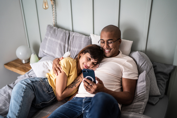Couple cuddling in bed looking at phone.
