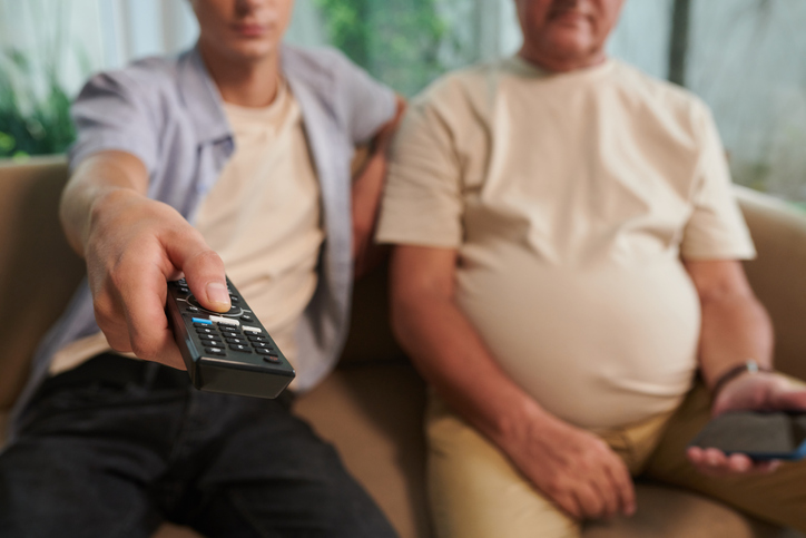 Two men sitting on couch watching TV.