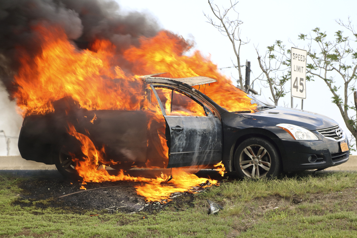 Car on fire on side of highway.
