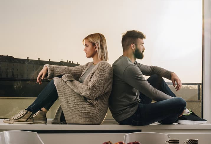 Sad couple ignoring each other while sitting back to back on a window sill.
