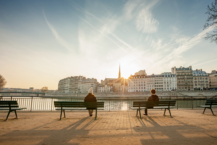 Two people sit on benches during sunset.