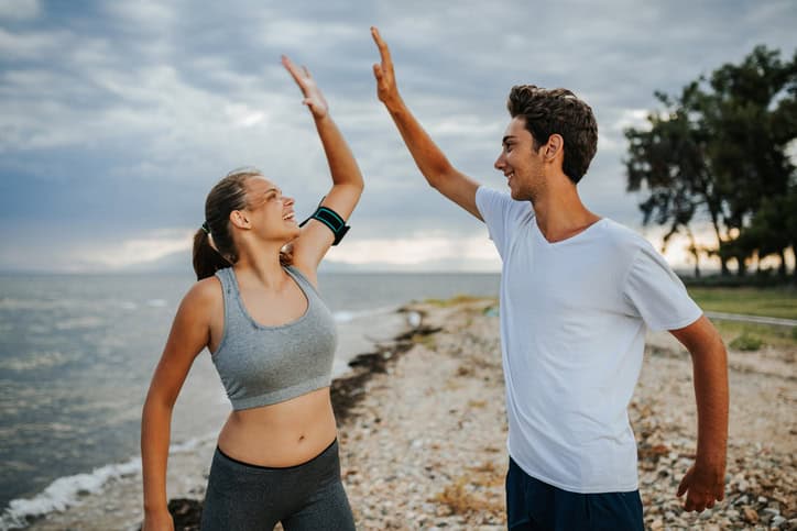 Beautiful young couple giving each other high five after hard training on the beach