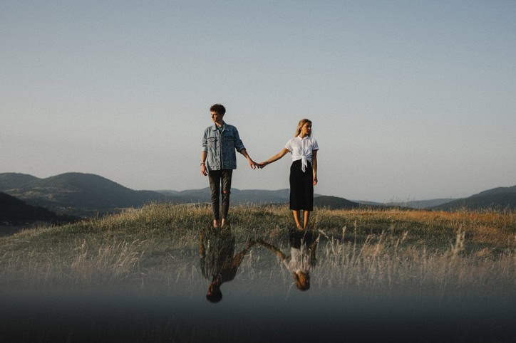 Young couple standing in nature in countryside, holding hands but looking away from each other.
